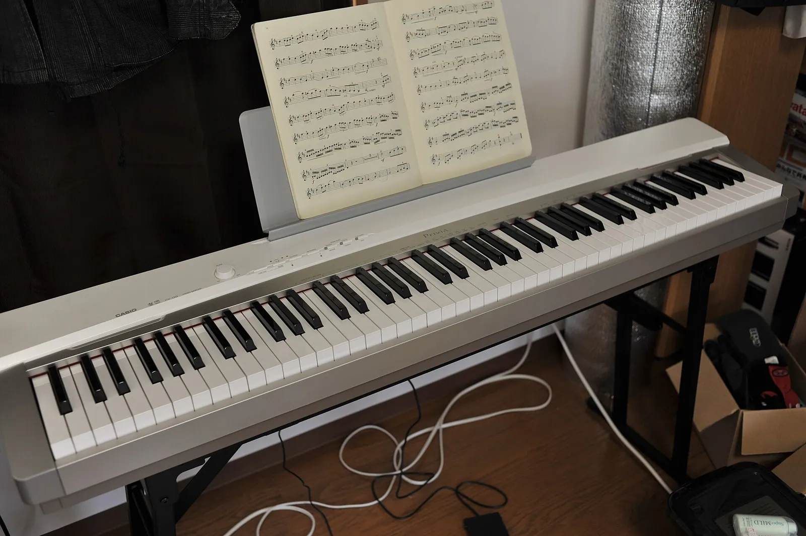 Piano digital portátil Casio Privia prateado sobre estante, com partitura aberta
