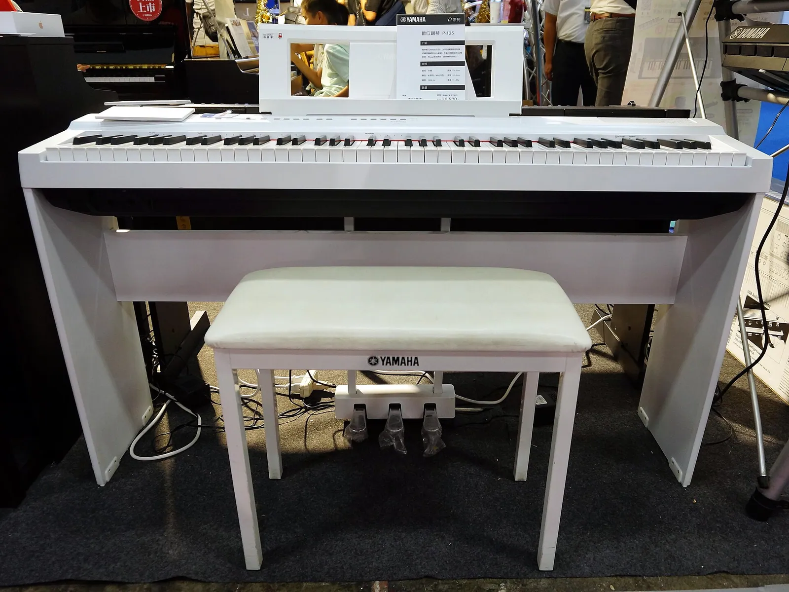 Piano digital portátil Yamaha branco sobre suporte de madeira, com banqueta e pedaleira de três pedais